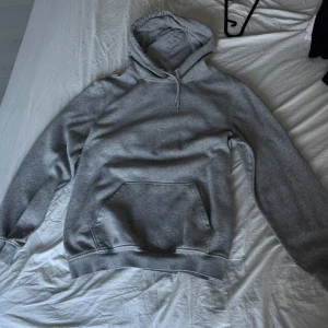 Grå hoodie från H&M Divided, storlek S - En klassisk grå hoodie från H&M Divided i storlek S. Tröjan har huva med snörning, magficka och är tillverkad i mjuk bomullsblandning. Perfekt för chill dagar eller när du vill ha något bekvämt och stilrent. Köpt på killavdelingen men alla kan använda den tycker jag. En av muddarna har liten skada men inte alls stor! 