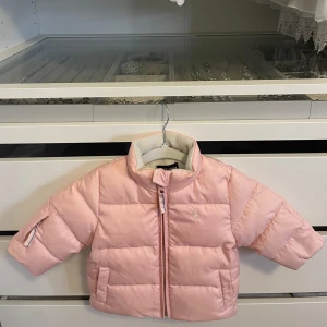 Ralph Lauren ljusrosa jacka - Supersöt ljusrosa pufferjacka från Ralph Lauren med dragkedja framtill, två fickor och mjukt fleecefoder på insidan. Perfekt för kyliga dagar.  Storlek: 9 månader.  Nypris över 2000kr.