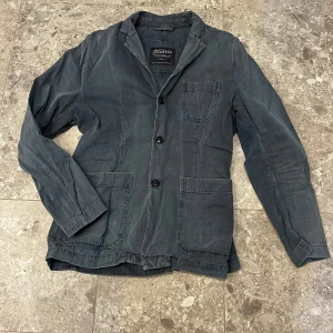 Grå blazer från Morris - Snygg mörkblå blazer från Morris med tre knappar framtill och tre praktiska fickor. Klassisk krage och enkel design som passar till många olika stilar. Skön känsla och för dig som gillar en avslappnad look.