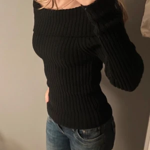 Svart ribbad offshoulder stickad tröja - Snygg svart stickad tröja med ribbat mönster och offshoulder-modell. Tröjan har lång ärm och sitter tight mot kroppen, perfekt till jeans eller kjol🫶🏼