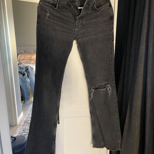 Svarta slitna jeans med hål - Svarta jeans med råa kanter och stort hål på ena knät. Jeansen har en utsvängd passform och är tillverkade i denim. Perfekta för dig som gillar en edgy och avslappnad stil.