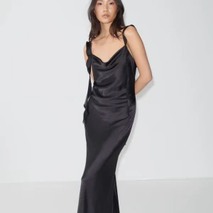 Svart långklänning i satin med knytband - Supersnygg svart långklänning i glansig satin med smala axelband och knytband. Klänningen har en draperad urringning och öppen rygg<3                                        Använd 1 gång                                                                                 Storlek 40 