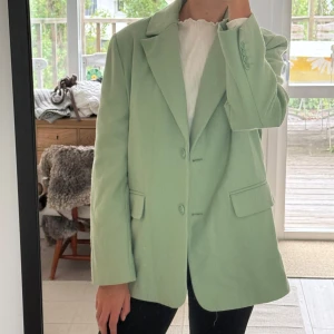 Ljusgrön kavaj från Envii - Snygg ljusgrön höstkavaj från Envii med klassisk krage, två knappar framtill och fickor med lock. Kavajen har en rak och lite oversized passform, perfekt att styla med stickad tröja eller t-shirt. Materialet är tjockt och mjukt och har en lätt struktur.