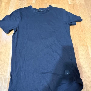 Svart t-shirt från Only & Sons - En basic svart t-shirt från Only & Sons i mjuk bomull. Modellen är klassisk med rund halsringning och korta ärmar. Liten svart logolapp nertill på framsidan. Perfekt till jeans eller shorts för en clean look.