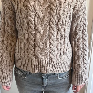 Beige kabelstickad tröja från H&M - Säljer en chunky beige kabelstickad tröja från H&M. Tröjan har grova flätmönster framtill och på ärmarna, samt ribbade muddar och nederkant. Perfekt för lager-på-lager och ger en mysig vibe till din outfit.