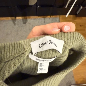 Olivgrön stickad tröja & Other Stories - Säljer en olivgrön stickad tröja från & Other Stories i 100% merinoull. Tröjan har kort ärm, ribbad struktur och en rundad hals. Snygg detalj med slits på sidorna som ger en chill vibe. Använd ett fåtal gånger💚