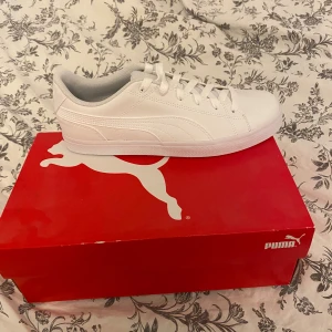 Vita Puma Court Point Vulc v2 sneakers - Fräscha helvita Puma Court Point Vulc v2 sneakers i klassisk låg modell. Skorna har stilren design med diskreta sömmar, snörning och rund tå. Tillverkade i syntetmaterial med platt sula för en clean look. Perfekta för dig som gillar minimalistisk stil.