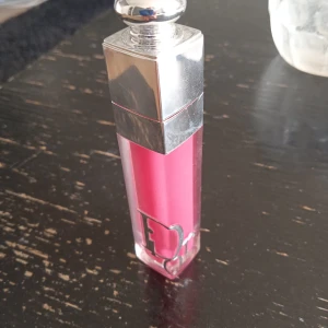 Dior rosa läppglans - Snyggt rosa läppglans från Dior med lyxig silverfärgad kork och genomskinlig hylsa. Perfekt för dig som vill ha glansiga och mjuka läppar med en poppig färg. Ikonisk Dior-logga på framsidan av förpackningen.