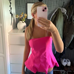 Rosa korsett topp med volang - Säljer en superfin rosa korsett topp med volangkant nedtill. Toppen har en snygg figurnära passform och axelband. Perfekt för dig som vill sticka ut med en färgstark och trendig look!