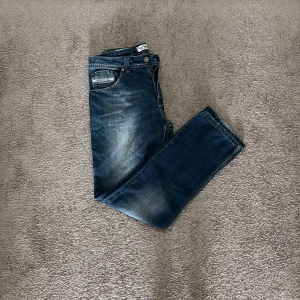 Blå jeans med slitningar - Säljer ett par snygga blå jeans med coola slitningar. De har en klassisk femficksdesign och en bekväm passform. Perfekta för en avslappnad stil! Passar mig som är 180 ungefär 