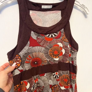 Mönstrad ärmlös topp från Promod - Säljer en färgglad ärmlös topp från Promod med ett coolt blommigt mönster i rött, orange och brunt. Perfekt för sommardagar eller en festlig kväll. Toppen har en rund halsringning och är i ett mjukt material.