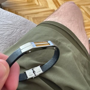 Stilrent armband i svart och silver - Säljer ett snyggt och modernt armband med en svart rem och detaljer i silver. Perfekt för att ge en stilren touch till din outfit. Armbandet har en enkel låsmekanism och passar bra till både vardag och fest.