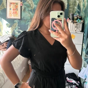 Svart miniklänning  - Supersöt svart miniklänning i tjockt tyg. Den har gulligt broderi i botten och fina ärmar. Den kommer med ett band att sätta i midjan så man kan göra en söt rosett i bak. Vet inte riktigt vilken storlek med tippar på S/M.