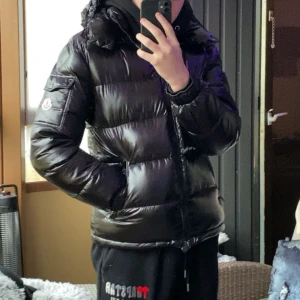 Svart pufferjacka från Moncler (Moncler maya) - Säljer en snygg och varm svart pufferjacka från Moncler. Jackan har en glansig finish och är perfekt för kalla vinterdagar. Jackan är i nyskick då jag endast använt den lite under 1 år (köptes i slutet av oktober 2023) och har en klassisk Moncler-logga på ärmen. Säljer den pågrund av att jag vill ha en billigare jacka så jag slipper vara lika försiktig. Hör av dig vid frågor eller om du vill ha fler bilder!