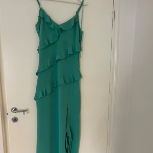 Blågrön klänning  - Blågrön klänning med volanger och slits. Går strax under vaden. Justerbara band