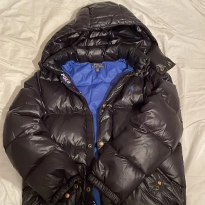 Ralph lauren dunjacka - Svart dunjacka från Ralph Lauren med huva och dragkedja. I storlek 14-16. Skick 10-10 använd ett par gånger.