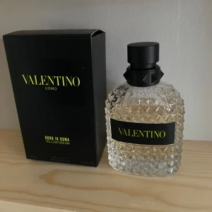 Valentino Uomo Born in Roma Yellow Dream - Elegant parfymflaska från Valentino med en lyxig design. Flaskan är genomskinlig med ett svart mönstrat lock och en svart etikett med gul text. Skriv om ni har några frågor eller en bättre bild för mängden. Priset är diskuterbart.