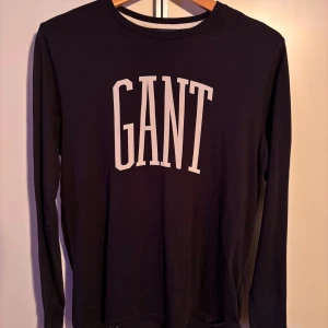 Svart långärmad tröja från GANT - Säljer en stilren marinblå långärmad tröja från GANT med vit logotyp på bröstet. Perfekt för en avslappnad och snygg look. Tröjan har rund hals och är superskön. Använd ett fåtal gånger.