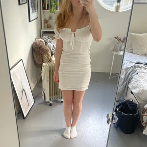 Vit offshoulder klänning - Säljer en söt vit offshoulder klänning med volangdetaljer och knyt framtill. Klänningen är kort och har en tight passform, perfekt för skolavslutningen eller student💗pris kan diskuteras 