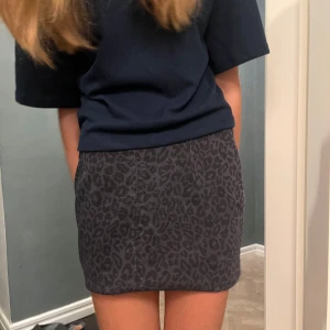 Grå och lilla leopardmönstrad kortkjol - Snygg grå kortkjol med leopardmönster. Perfekt för en trendig look. Kjolen har en enkel design utan extra detaljer, vilket gör den lätt att matcha med olika toppar.