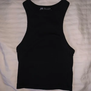 Svart ribbad linnetopp från Zara - Snygg svart ribbad linnetopp från Zara. Perfekt för en stilren look med sin ärmlösa design och rundade halsringning. Passar utmärkt till både jeans och kjol.