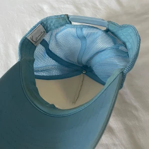 Vit och blå keps med broderad text - Snygg keps i Vit och blått med broderad text framtill. Kepsen har ett nätmaterial baktill för extra ventilation och en justerbar rem för perfekt passform.