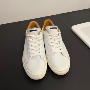 Vita sneakers från pepejeans - Snygga vita sneakers från Pepe jeans med klassisk design. Skorna har snörning och en diskret logga på sidan. Perfekta för en stilren look. Negativt är att de inte är original sulan, finns lite tecken på användning men annars är dom i bra sick