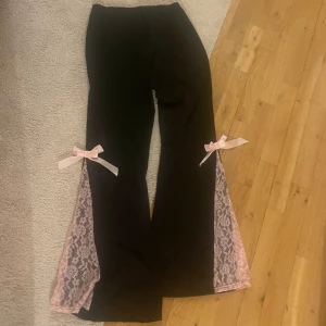 Svarta byxor med rosa spets och rosetter - Unika svarta byxor med rosa spetsdetaljer längs benen och söta rosett. Aldrig använda och storlek L❤️