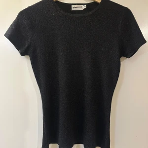 Svart glittrig topp från Gina Tricot - Snygg svart glittrig topp från Gina Tricot med korta ärmar. Perfekt för en kväll ute eller en festlig tillställning. Toppen har en rund halsringning och en figurnära passform.🌟