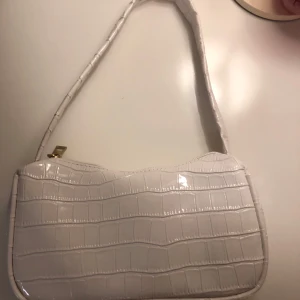 Vit axelväska i syntet - Snygg vit axelväska i syntet med krokodilpräglat mönster och guldfärgad dragkedja. Perfekt för att ge en stilren touch till din outfit.