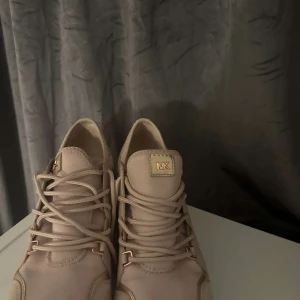 Ljusrosa sneakers från Michael Kors - Snygga ljusrosa sneakers från Michael Kors med snörning och gulddetaljer. Skorna har en vit sula och är perfekta för en stilren look.