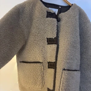 Beige teddyjacka från Carin Wester - Mysig beige jacka i pälsimitation från Carin Wester med klädda knappar framtill. Fickor framtill. Som ny, använd ett fåtal gånger. Finns i butik nu. Nypris 1499kr. 