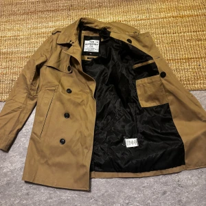 Brun trenchcoat från Superdry - Snygg brun trenchcoat från Superdry med dubbelknäppning och klassisk krage. Jackan har långa ärmar och två framfickor. Perfekt för höst och vår. Modellen heter Remastered rouge, den är i Size S och skicket 10/10. Nypris ligger på 1699:-. Färgen på första bilden är så som den ser ut irl.