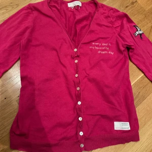 Rosa kofta Odd Molly - Fin rosa kofta från Odd Molly med broderad text 'every day is my favorite dream day' på framsidan. Koftan har knappar framtill och ett broderat märke på ärmen. Dragkedja längst ner på ärmarna