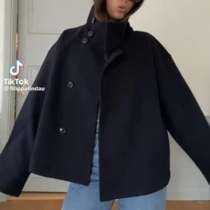 SVART kappa med hög krage - !SVART! kappa med hög krage och knappar framtill. Jackan har en modern, croppad design med långa ärmar och breda muddar. Perfekt för en stilren look. Nypris 600kr
