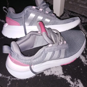 Grå och rosa sneakers från Adidas - Snygga grå sneakers med rosa detaljer från Adidas. Skorna har en vit sula och klassiska tre ränder i silver på sidan. Perfekta för en sportig look. Storlek 36.5 Adidas . Nike 37.5 . 