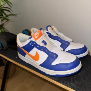 Nike Dunk i blått och orange - Snygga Nike Dunk sneakers i en fräsch färgkombination av blått, vitt och orange.  De är köpta i USA aldrig använt mer en 1 gång. Snörarna ligger tillsammans med lådan! Väldigt fina skor. Nypris 2300kr. Kontakta för intresse och frågor. Priset kan alltid diskuteras! 