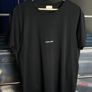 Svart t-shirt från Saint Laurent - Snygg svart t-shirt från Saint Laurent med ett diskret tryck av märkesnamnet på bröstet. Perfekt för en stilren look. Storlek XL sitter som en L 