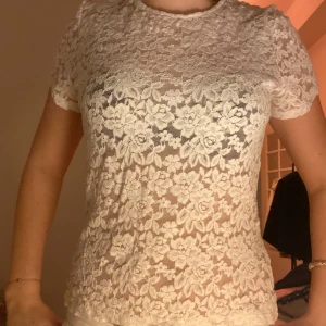 Vit spetsblus - Säljer en elegant vit spetsblus med korta ärmar. Blusen har ett vackert blommönster och är perfekt för en stilren look. Passar bra till både jeans och kjol.