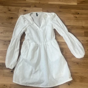 Vit klänning från H&M - Söt vit klänning från H&M med broderade blommor och v-ringning. Klänningen har långa ärmar och en elastisk midja för en bekväm passform. Perfekt för vår och sommar! Säljer pga för liten