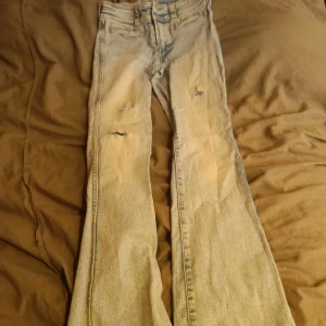 Ljusblå bootcut jeans - Säljer ett par ljusblå bootcut jeans med slitna detaljer på framsidan. Jeansen har en klassisk femficksdesign och är perfekta för en avslappnad stil. De har en bekväm passform och är tillverkade i denim.