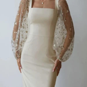 Vit klänning med broderade ärmar från Cherley - Elegant vit klänning med fyrkantig urringning och långa, transparenta ärmar dekorerade med blommiga broderier. Perfekt för speciella tillfällen med sin stilrena design och fina detaljer. Aldrig använt gick ej returnera , tänkte ha på student men hittade en annan.