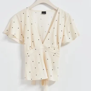 Beige prickig topp från Gina tricot - Säljer nu min sååå snygga beige blus från Gina Tricot med svarta prickar och v-ringning. Blusen har korta ärmar och en knytning i midjan som ger en fin passform. 