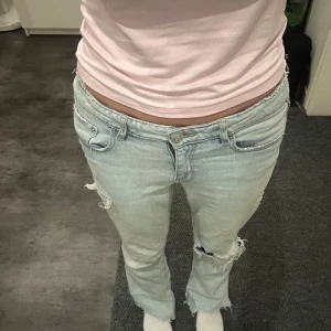 Ljusblå jeans från Gina Tricot - Säljer ett par ljusblå jeans från Gina Tricot. De har en avslappnad passform med slitna detaljer på knäna och en bootcut-stil. Perfekta för en casual look!