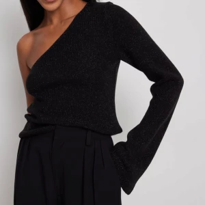 Svart glittrig oneshoulder topp från NA-KD - Svart glittrig topp från NA-KD med oneshoulder-design och långa ärmar. Storlek S. 