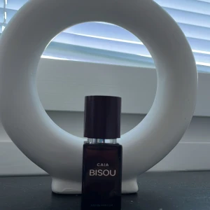 Parfym CAIA Bisou - Säljer en elegant parfymflaska från CAIA med doften Bisou. Flaskan är mörk och stilren med en svart kork. Perfekt för den som vill ha en sofistikerad doftupplevelse.
