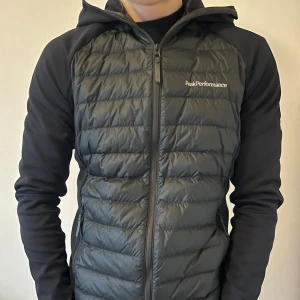 Svart cardigan Peak Performance - Säljer en svart vår/höst jacka från Peak Performance med dragkedja och huva. Jackan har långa ärmar och passar perfekt om man är mellan 175cm-185cm ungefär. Den har inga som helst skador eller slitage. Exakta modellen säljs inte längre nya, men liknande plus denna ligger runt 2500kr.