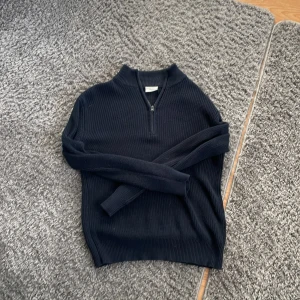 Svart ribbad tröja från Grunt - Säljer en stilren svart ribbad tröja från Grunt med dragkedja vid halsen. Perfekt för kyligare dagar och enkel att matcha med olika outfits. Tröjan har långa ärmar och en bekväm passform.👍