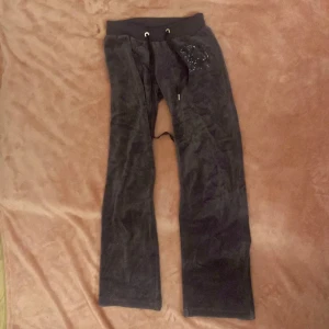 Lila mjukisbyxor från Juicy Couture - Säljer ett par lila mjukisbyxor från Juicy Couture. Byxorna har en glittrig detalj med en katt på ena benet och är tillverkade i en mjuk bomulls- och polyesterblandning. Perfekta för en avslappnad stil med en bekväm passform.