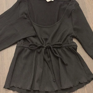 Svart ribbad topp med knytband - Svart topp från Nelly. Använd 1 gång.